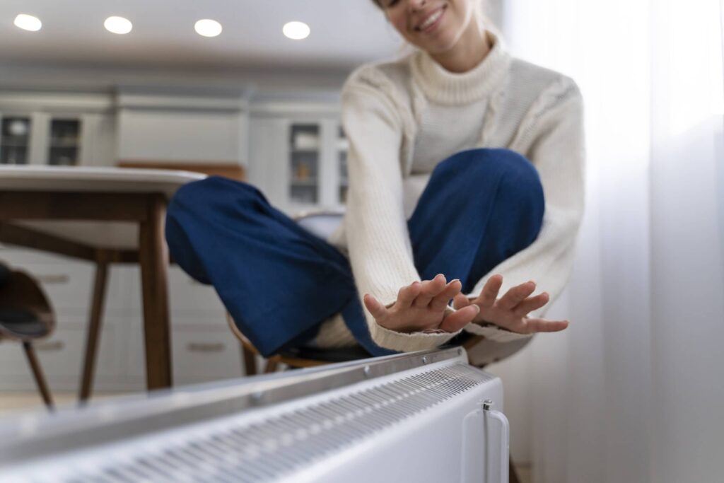 Une femme se réchauffe à un radiateur électrique, profitant de la chaleur confortable en hiver pour rester au chaud et à l'aise.