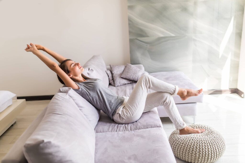 Une femme assise confortablement dans un fauteuil, profitant de la fraîcheur de la climatisation de sa maison tout en lisant un livre et en se relaxant.