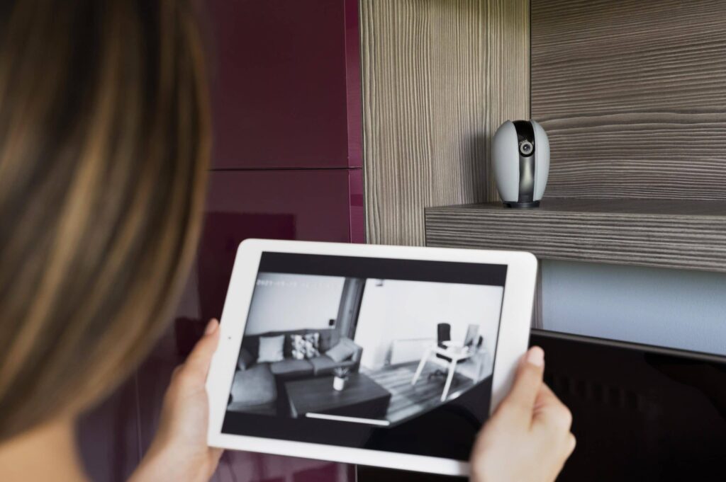 Jeune femme tenant une tablette, affichant en temps réel l'intérieur de sa maison via la caméra de surveillance. Contrôle à distance et tranquillité d'esprit dans le creux de la main.